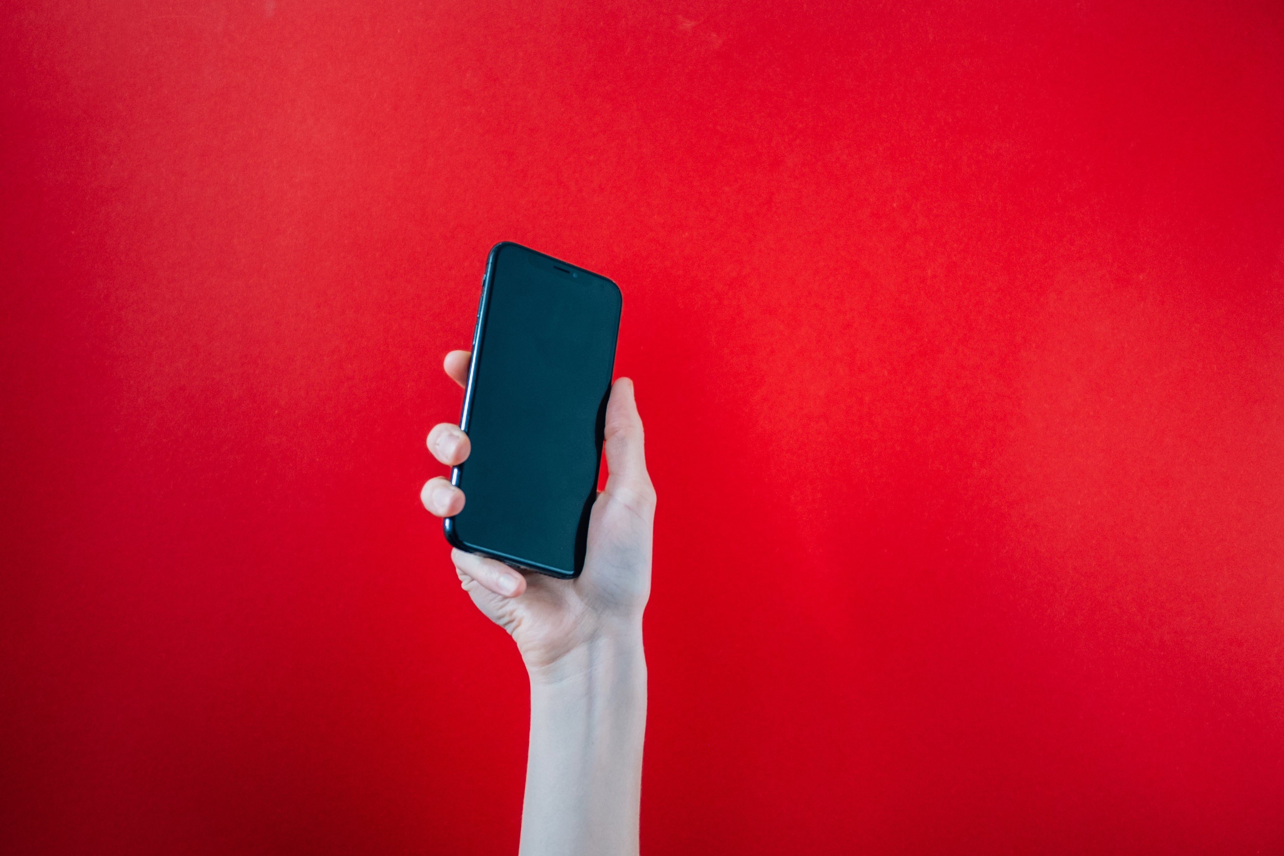 hand-holds-up-black-mobile-phone-on-red-background.jpg